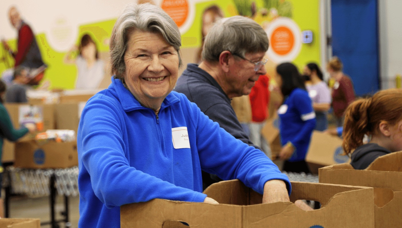 An Atlanta Community Food Bank volunteer smiling beside a stack of donation boxes