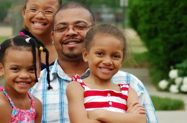 A father smiling with his three young daughters